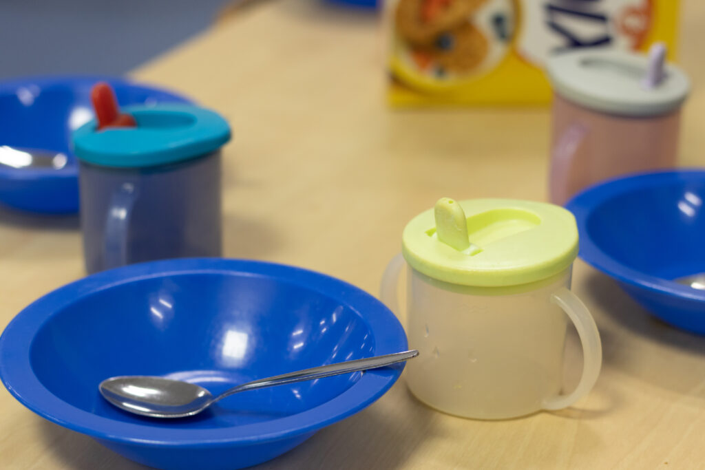 Close up of plastic bowl, metal spoon and spout cup in the dining area of the nursery.