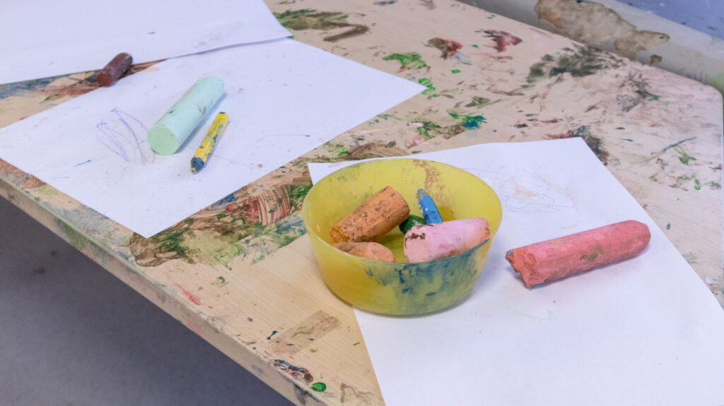 different coloured chalk and paper on a wooden, paint-stained drawing table in the nursery.