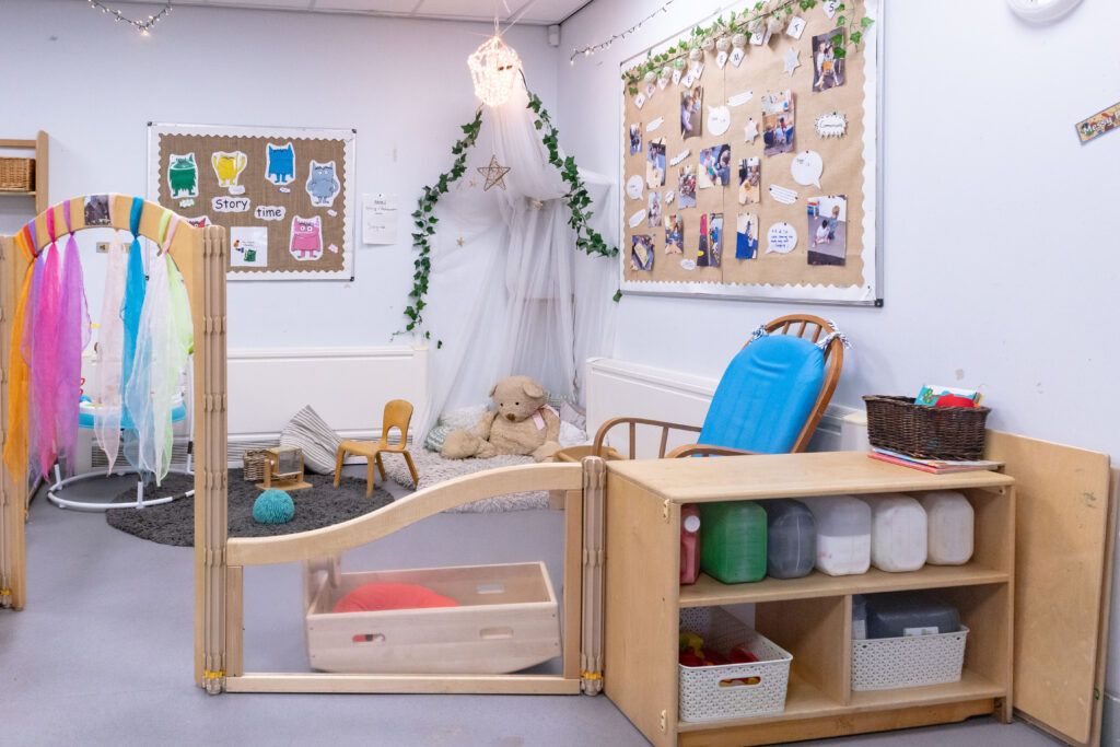 Cosy area of three months to two years section of nursery. There are chairs, cushions and toys such as a teddy and baby jumper.
